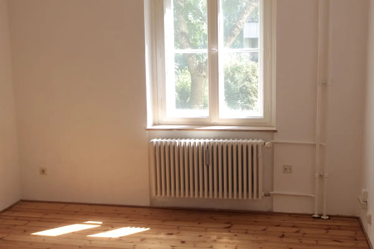Pièce vide d'un logement ancien : plinthes, parquet et radiateur, refuges classiques des nuisibles